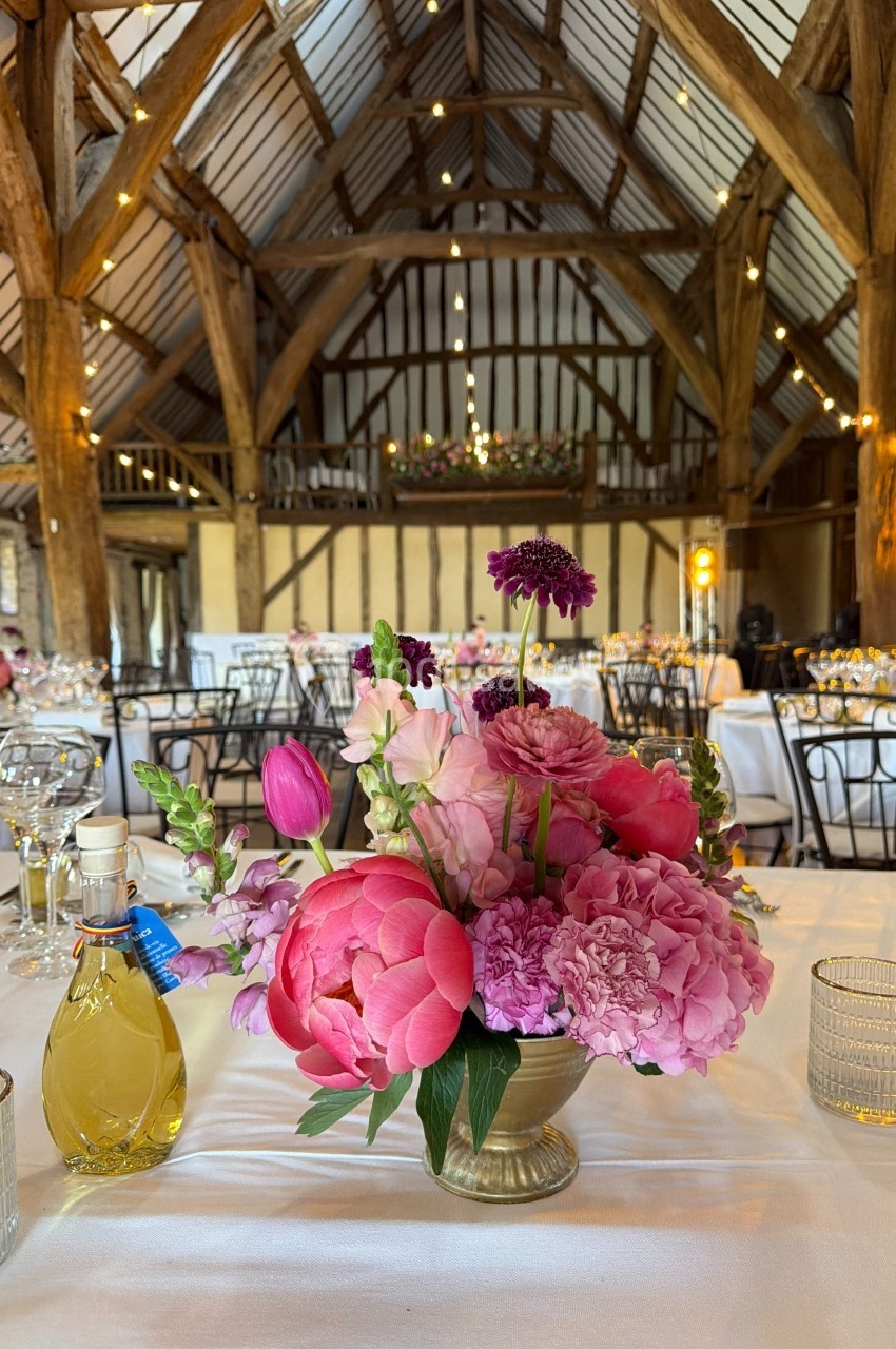 Centre de table fleuri avec pivoines roses et tulipes, dans une salle en bois avec poutres apparentes et éclairage…