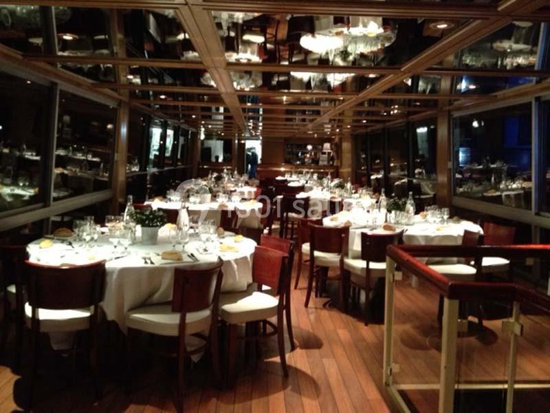 Salle de restaurant élégante avec tables rondes dressées, chaises en bois et plafond réfléchissant.