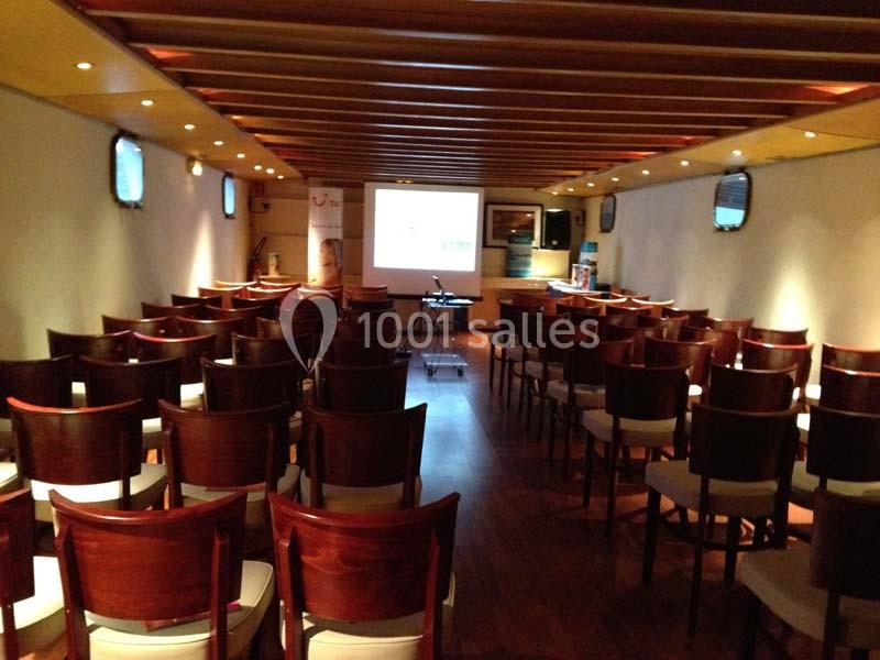 Salle de conférence avec des rangées de chaises en bois, un écran de projection et un projecteur allumé.
