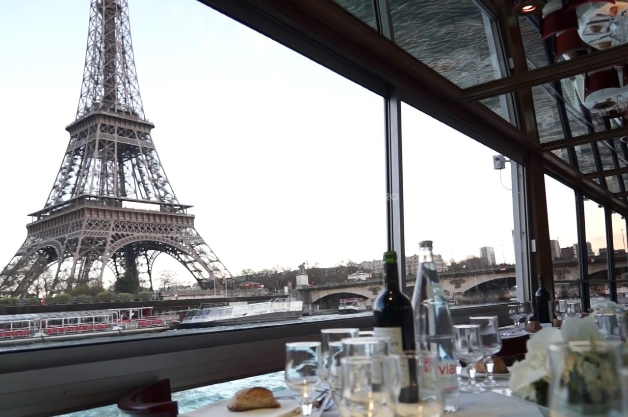 Vue de la Tour Eiffel depuis l'intérieur d'un restaurant avec une table dressée et des verres en premier plan.
