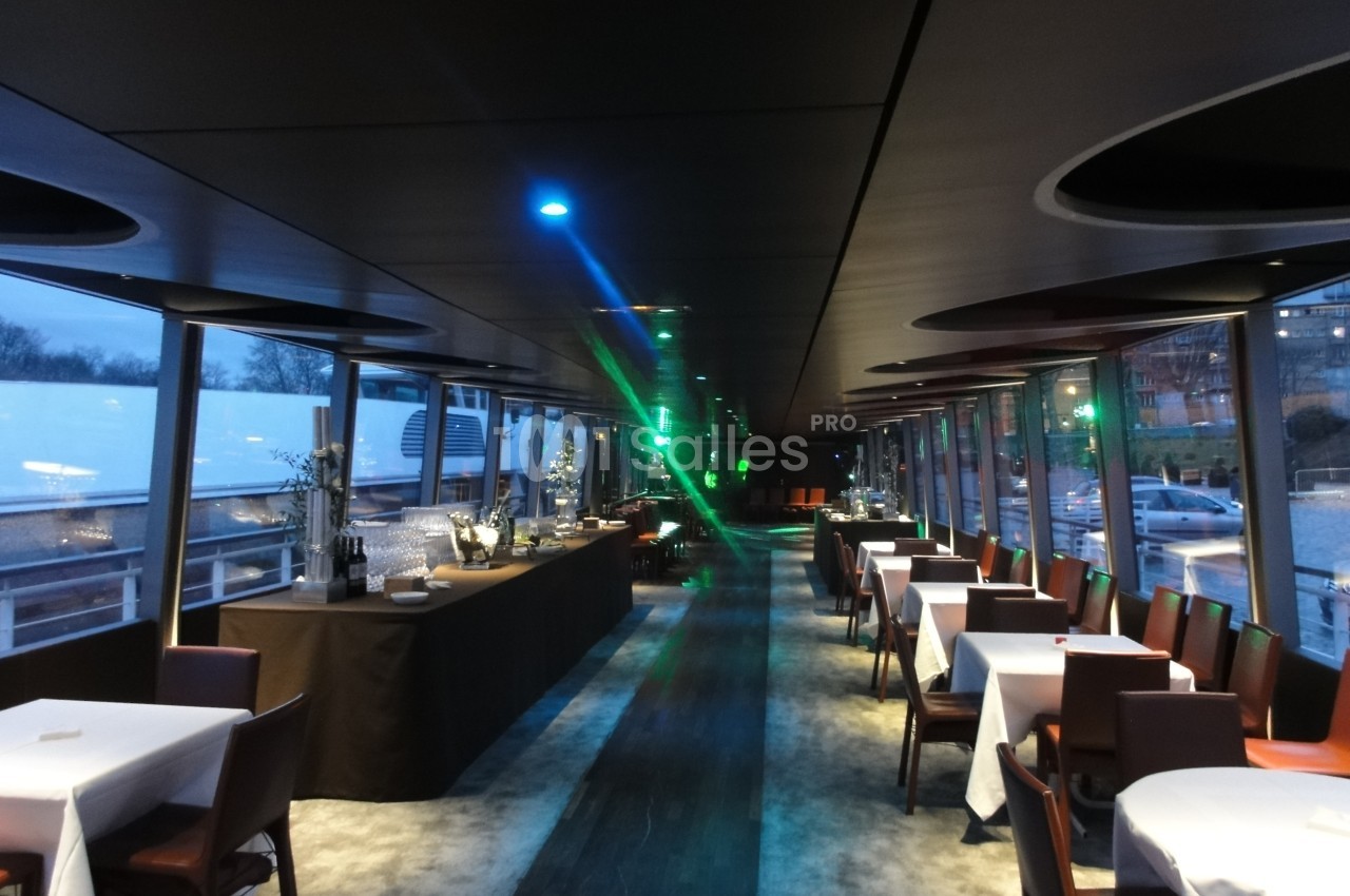 Salle de restaurant moderne avec tables dressées, buffet à gauche et grandes baies vitrées donnant sur l'extérieur.