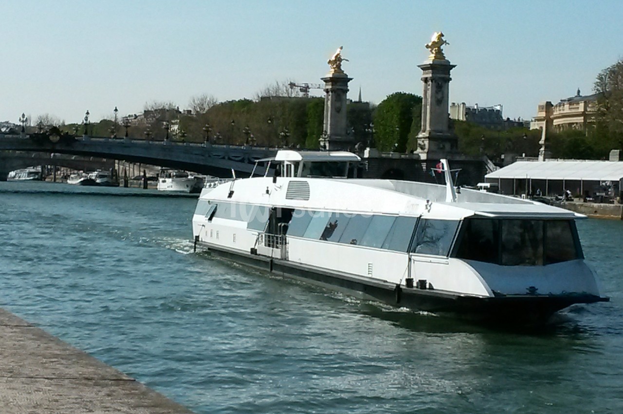 Bateau moderne naviguant sur une rivière avec un pont orné de sculptures dorées en arrière-plan.