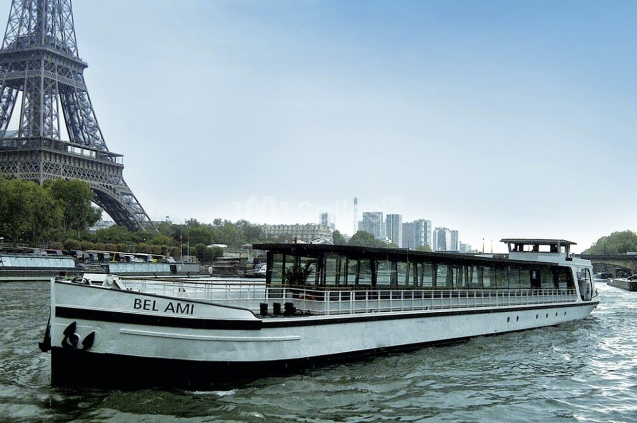 Bateau de croisière ’Bel Ami’ naviguant sur la Seine, avec la tour Eiffel et des arbres en arrière-plan.