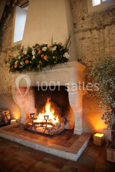 Cheminée en pierre allumée, décorée de fleurs et entourée de murs en pierre dans une ambiance chaleureuse.