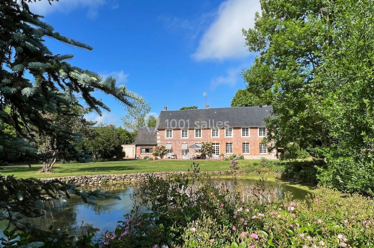 Grande maison en briques rouges entourée d'un jardin verdoyant avec un étang au premier plan.
