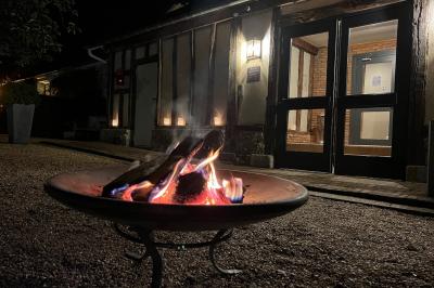 Brasero allumé dans une cour gravillonnée devant un bâtiment éclairé avec des murs en bois et des portes vitrées.