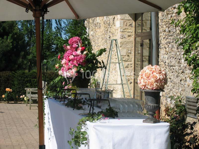 Table décorée avec des fleurs roses et blanches sous un parasol, près d'un mur en pierre dans un jardin ensoleillé.