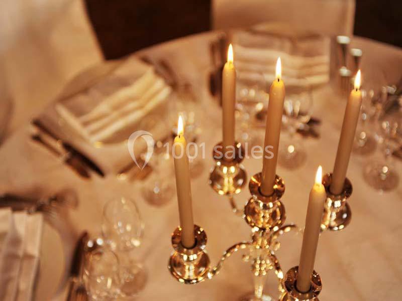 Chandelier doré avec bougies allumées sur une table élégamment dressée avec nappes et verres.