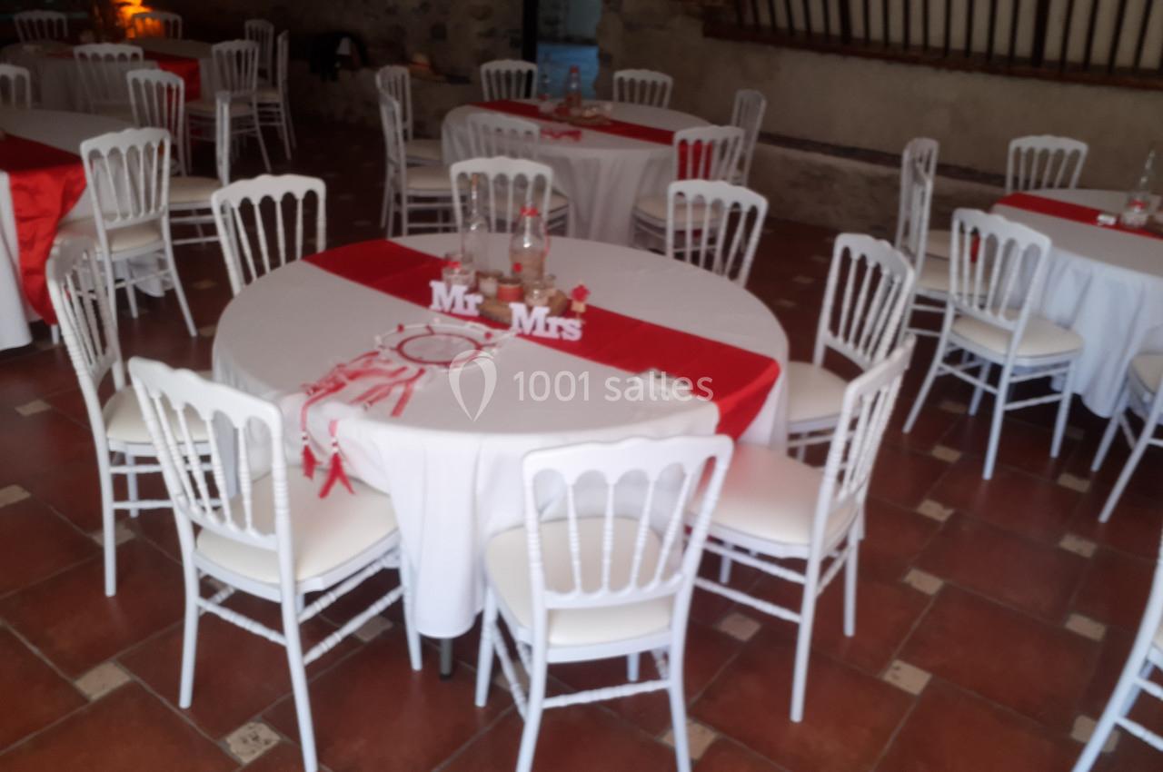 Salle décorée pour un mariage avec des tables rondes recouvertes de nappes blanches et chemins de table rouges.