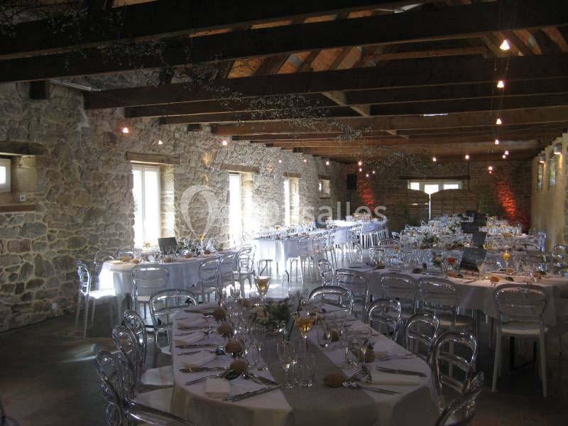 Location salle Douarnenez (Finistère) - La Ferme de Trézulien #11 Salle en pierre avec poutres apparentes, tables rondes dressées pour un événement, chaises transparentes et lumière…