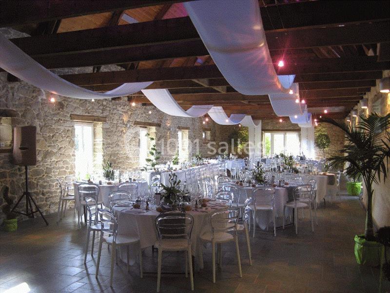 Location salle Douarnenez (Finistère) - La Ferme de Trézulien #13 Salle de réception en pierre avec tables dressées, chaises transparentes et décoration suspendue en tissu blanc.