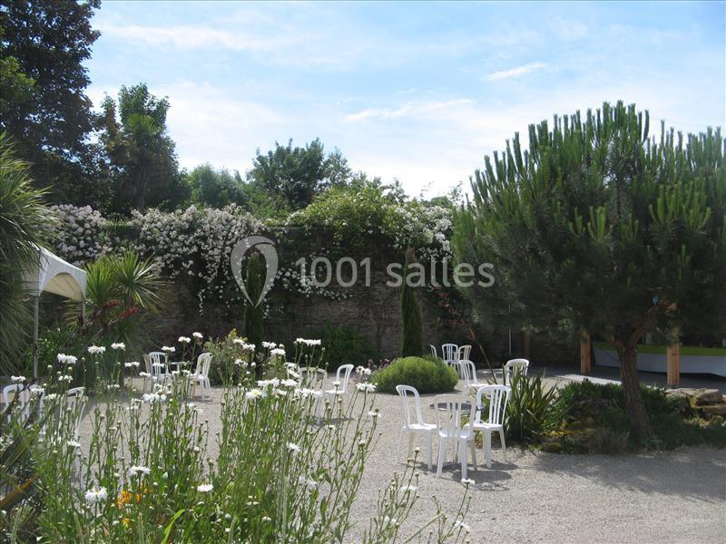 Location salle Douarnenez (Finistère) - La Ferme de Trézulien #23 Jardin avec des fleurs blanches, des chaises en plastique dispersées et des arbres sous un ciel partiellement dégagé.