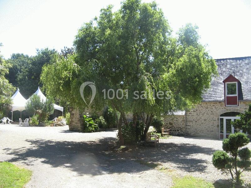 Location salle Douarnenez (Finistère) - La Ferme de Trézulien #19 Cour avec un grand arbre au centre, entourée de bâtiments en pierre et de tentes blanches en arrière-plan.