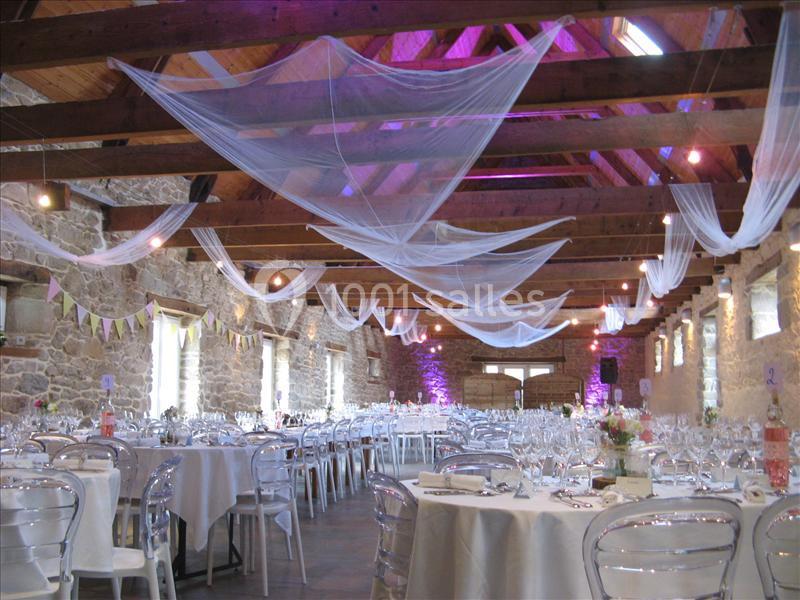 Location salle Douarnenez (Finistère) - La Ferme de Trézulien #2 Salle de réception en pierre avec tables dressées, chaises transparentes et voilages suspendus au plafond en bois.