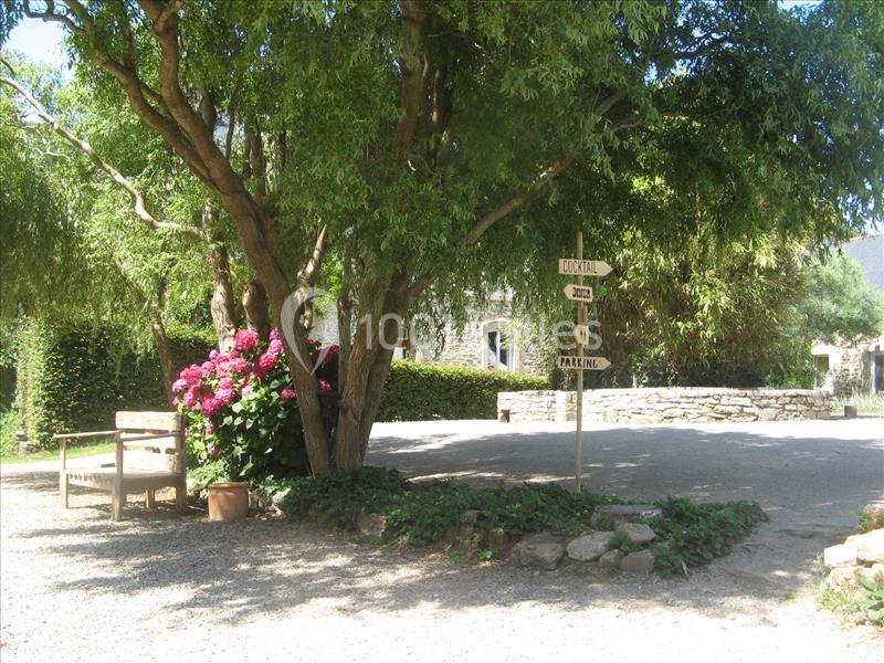 Location salle Douarnenez (Finistère) - La Ferme de Trézulien #24 Allée ombragée avec banc en bois, hortensias en fleurs et panneaux directionnels près d'un arbre.