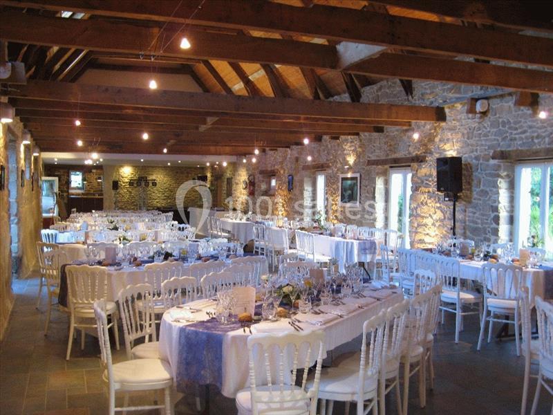 Location salle Douarnenez (Finistère) - La Ferme de Trézulien #15 Salle de réception en pierre avec poutres apparentes, tables dressées et chaises blanches pour un événement.