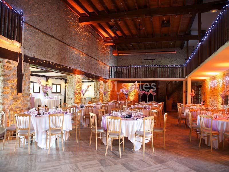 Salle de réception en pierre avec plafond en bois, tables rondes dressées et décorations lumineuses suspendues.