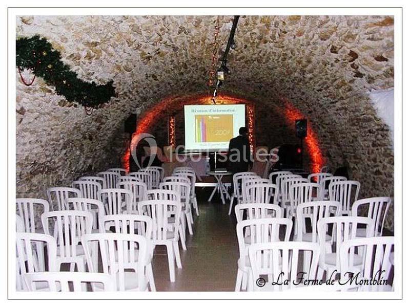 Salle voûtée en pierre avec des rangées de chaises blanches disposées face à un écran de projection allumé.