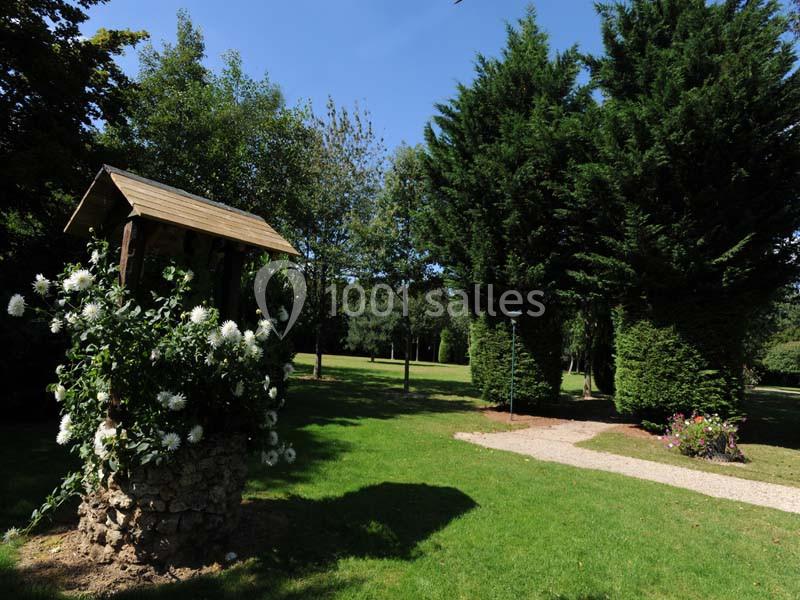 Un puits fleuri entouré de pelouse et d'arbres dans un jardin sous un ciel dégagé.
