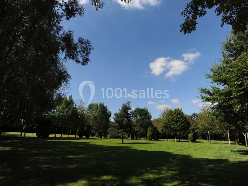 Pelouse verdoyante entourée d'arbres sous un ciel bleu parsemé de quelques nuages.