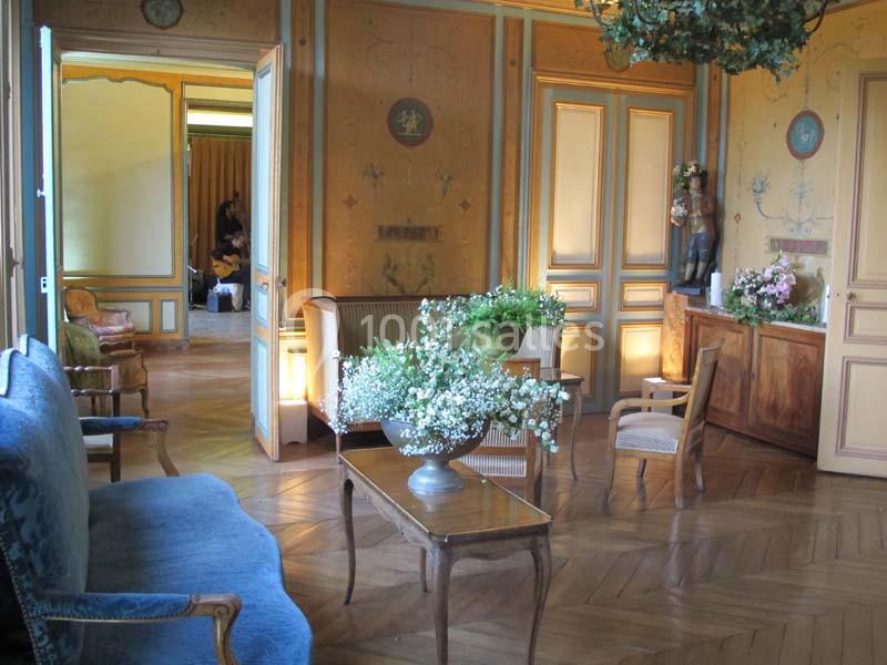 Salon élégant avec parquet en bois, mobilier classique, fleurs décoratives et murs ornés de motifs peints.