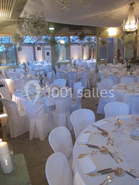Salle de réception décorée avec des tables rondes dressées, nappes blanches et chaises assorties, ambiance lumineuse.