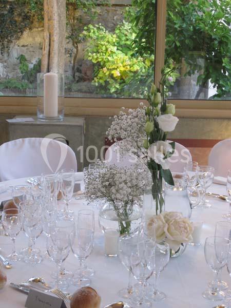 Table élégamment dressée avec nappes blanches, verres, bougies et un centre de table floral dans un cadre lumineux.