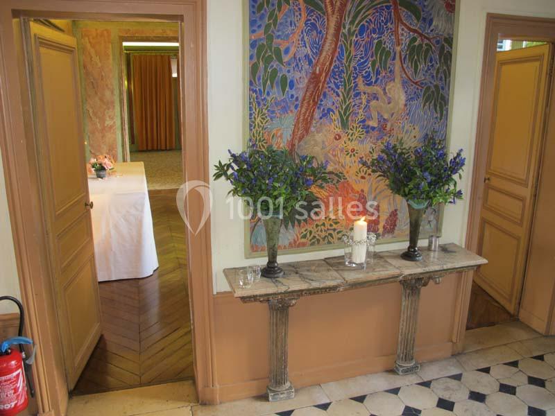 Console en marbre avec deux vases de fleurs violettes et une bougie, devant un mur décoré d'une peinture colorée.
