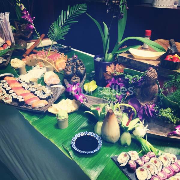 Buffet décoratif avec sushis, fleurs exotiques, statues et feuilles vertes servant de nappes.