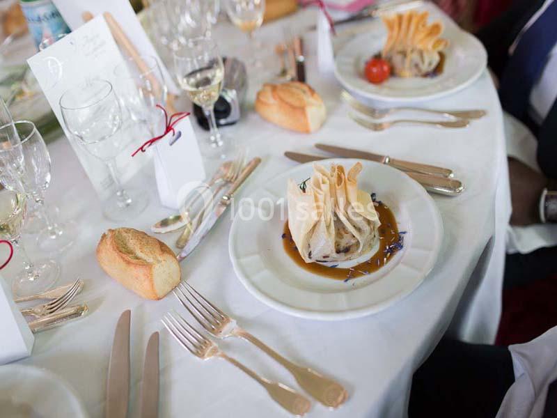 Assiette dressée avec une aumônière sur sauce, entourée de couverts, pain et verres sur une table de réception.