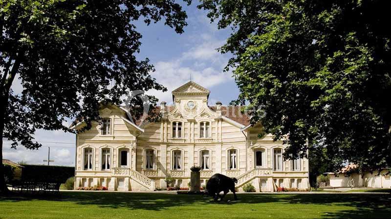 Location salle Moulis-en-Médoc (Gironde) - Château Maucaillou #14 Façade d'un manoir en pierre claire entouré d'un jardin verdoyant, sous un ciel partiellement nuageux.