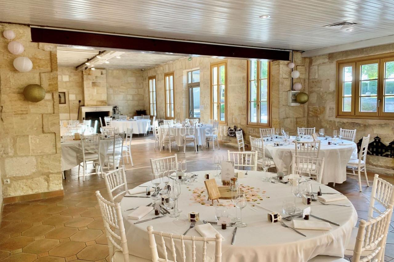 Location salle Moulis-en-Médoc (Gironde) - Château Maucaillou #19 Salle de réception lumineuse avec murs en pierre, tables rondes dressées et chaises blanches, décorée pour un événement.