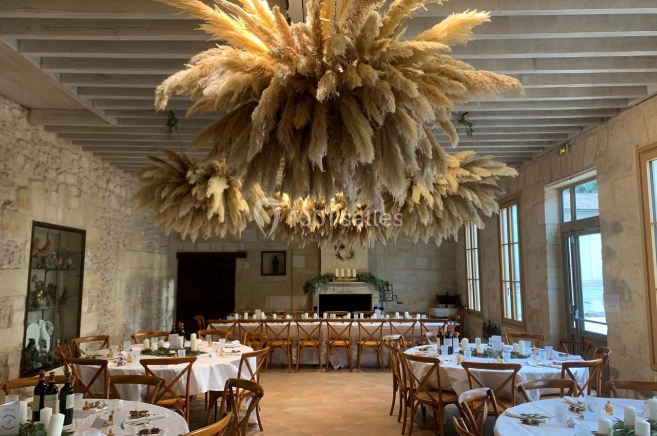 Location salle Moulis-en-Médoc (Gironde) - Château Maucaillou #18 Salle de réception avec tables dressées et grande suspension décorative en herbes séchées au plafond.