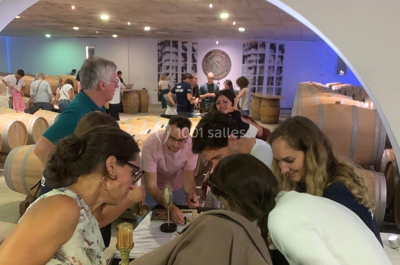 Location salle Moulis-en-Médoc (Gironde) - Château Maucaillou #8 Des visiteurs observent une démonstration dans une cave à vin, entourés de tonneaux en bois et d'une ambiance lumineuse.