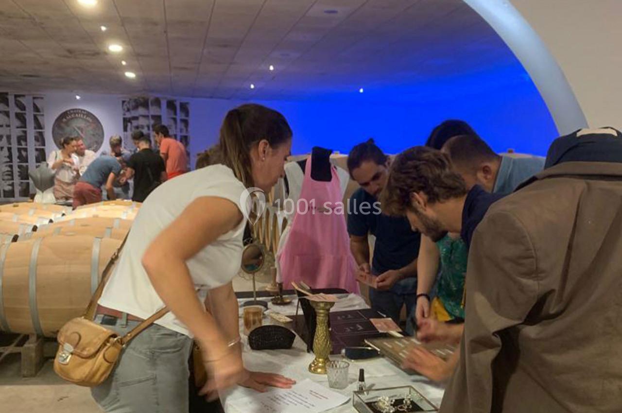 Location salle Moulis-en-Médoc (Gironde) - Château Maucaillou #6 Des personnes participent à une activité interactive autour d'une table dans une cave à vin, entourées de tonneaux.
