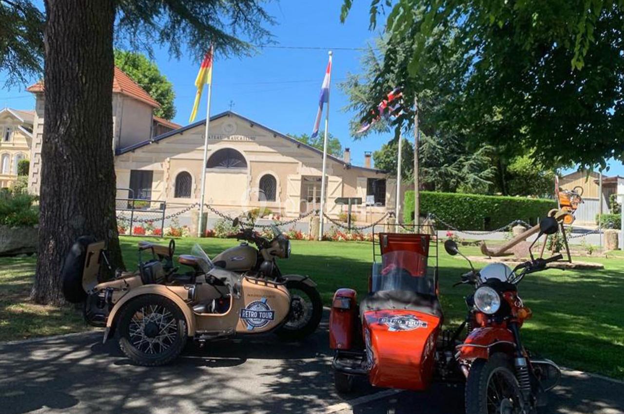 Location salle Moulis-en-Médoc (Gironde) - Château Maucaillou #25 Deux motos avec side-cars stationnées devant un bâtiment ancien entouré d'arbres et de drapeaux.