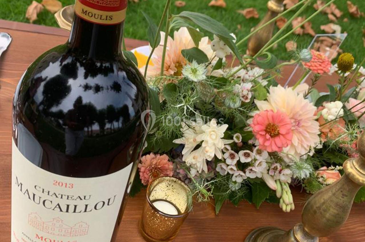 Location salle Moulis-en-Médoc (Gironde) - Château Maucaillou #24 Bouteille de vin rouge Château Maucaillou 2013 posée sur une table en bois avec un bouquet de fleurs et des bougeoirs.
