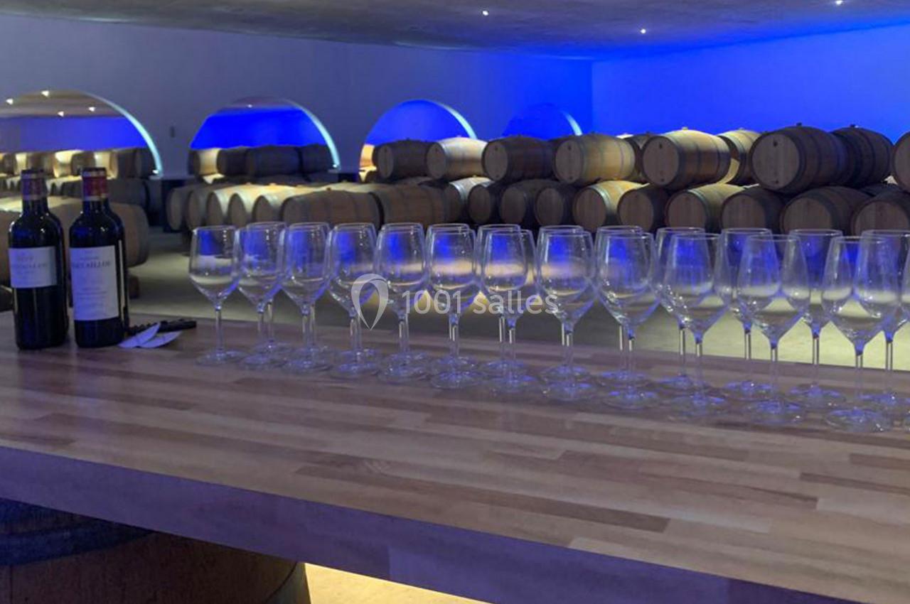 Location salle Moulis-en-Médoc (Gironde) - Château Maucaillou #5 Rangée de verres à vin vides sur un comptoir en bois, avec des barriques et deux bouteilles en arrière-plan.