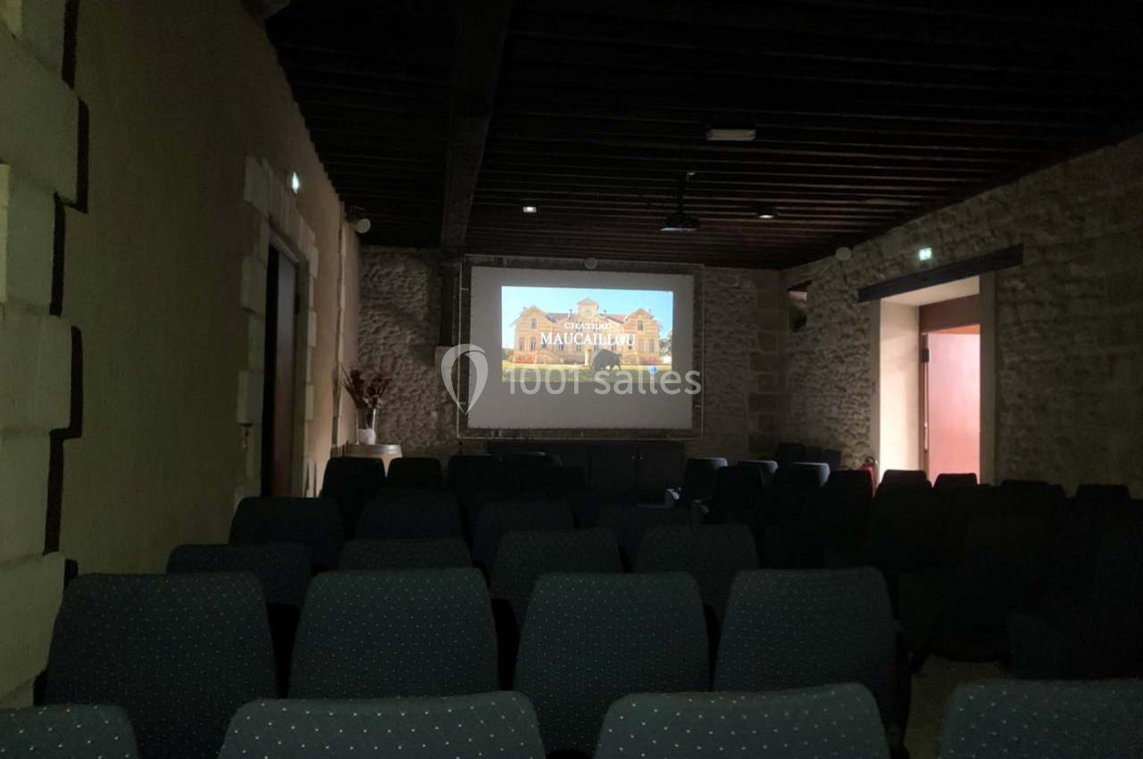 Location salle Moulis-en-Médoc (Gironde) - Château Maucaillou #12 Salle sombre avec rangées de sièges vides, écran de projection affichant une image d'un bâtiment ancien.