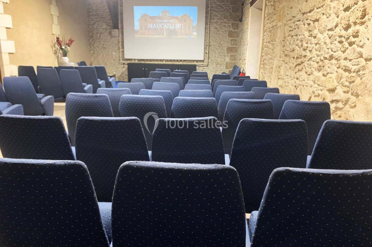 Location salle Moulis-en-Médoc (Gironde) - Château Maucaillou #11 Salle de conférence avec des rangées de sièges bleus et un écran de projection affichant une image.