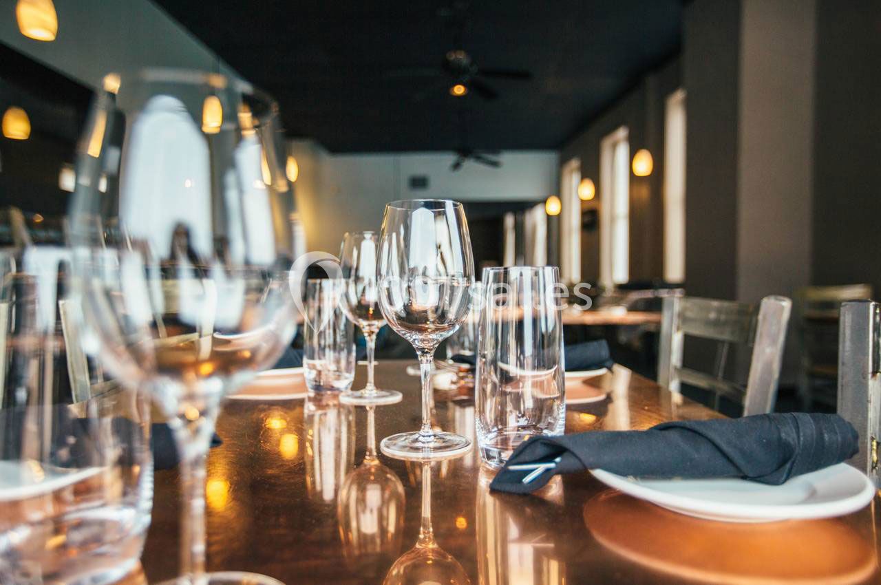 Table dressée dans un restaurant avec verres, assiettes blanches et serviettes noires sur une surface en bois.