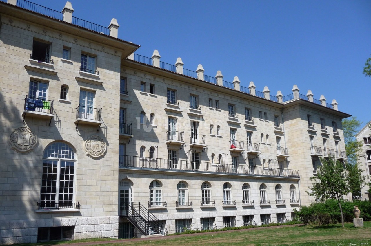 Bâtiment en pierre de style classique avec balcons, grandes fenêtres et un espace vert au premier plan.