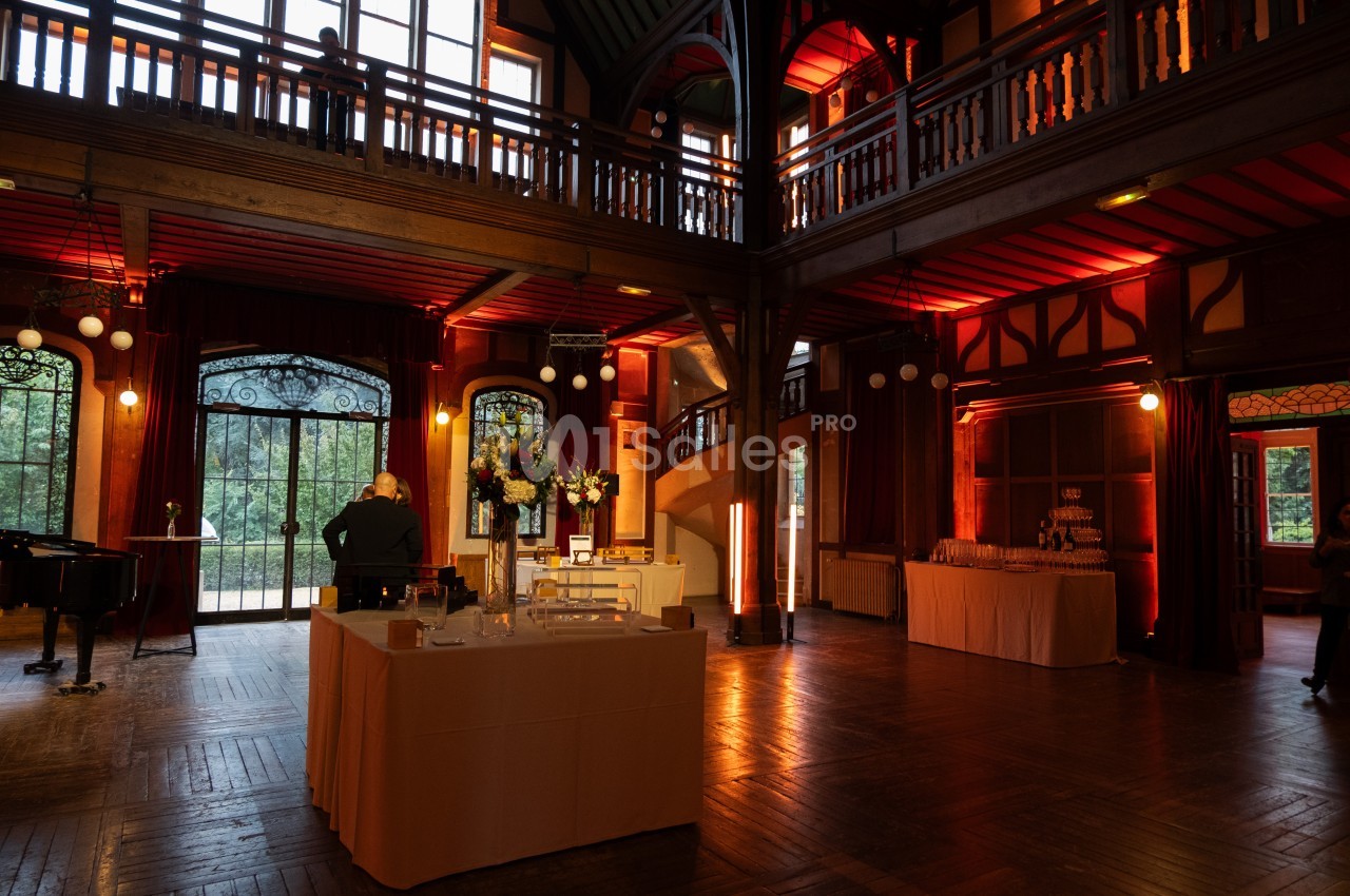 Salle en bois avec éclairage chaleureux, tables dressées et grandes fenêtres donnant sur un extérieur verdoyant.
