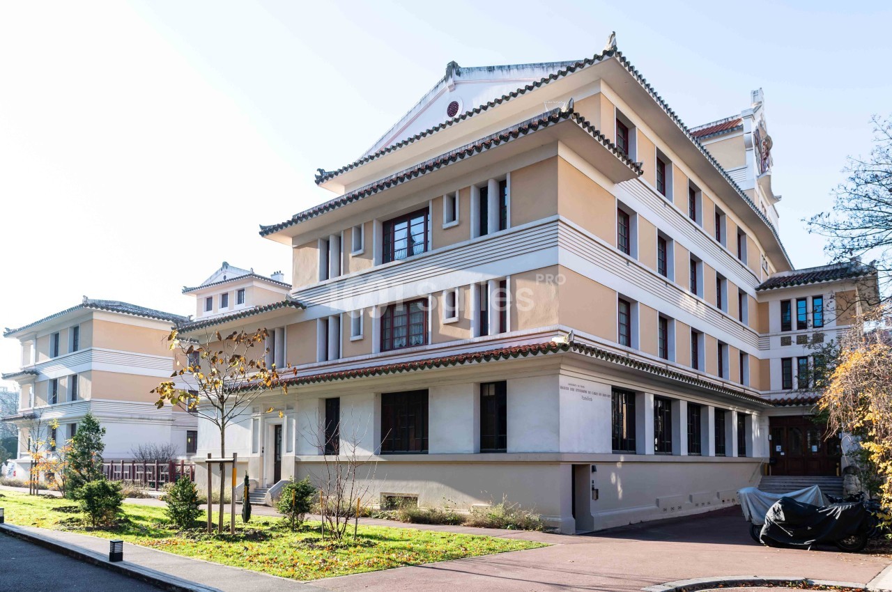 Bâtiment de style asiatique avec plusieurs étages, toits en pagode et façade beige, entouré d'arbres et d'un trottoir.