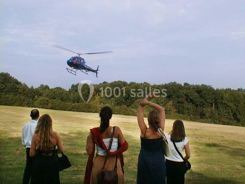 Un hélicoptère en vol au-dessus d'un champ, observé par un groupe de personnes debout au premier plan.