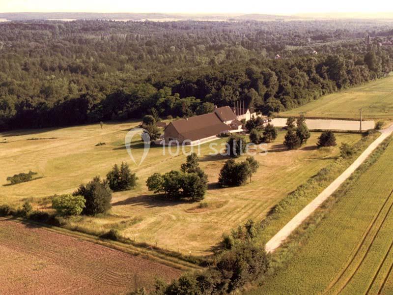 Vue aérienne d'une ferme entourée de champs et d'arbres, avec une route traversant le paysage rural.
