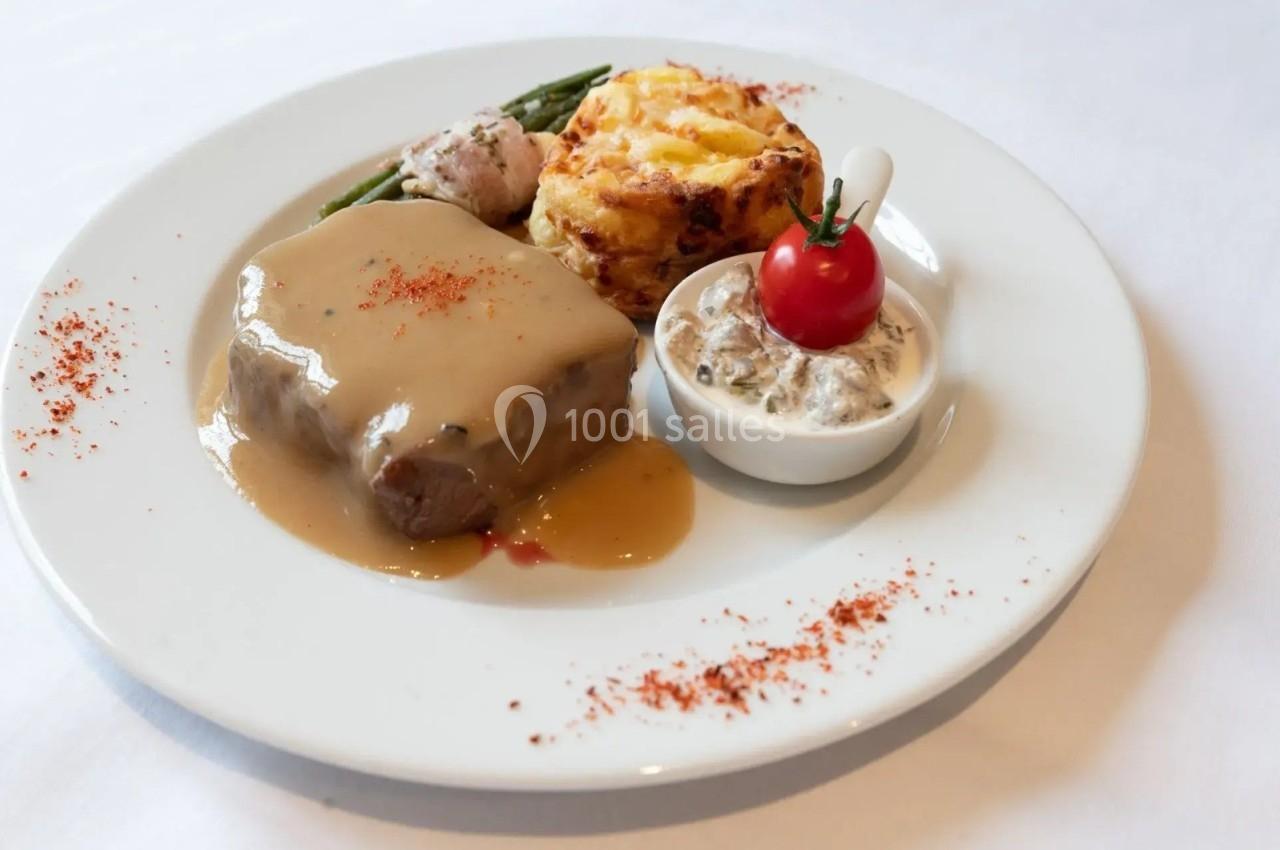 Assiette composée d'une viande nappée de sauce, gratin, haricots verts, tomate cerise et accompagnement en sauce.