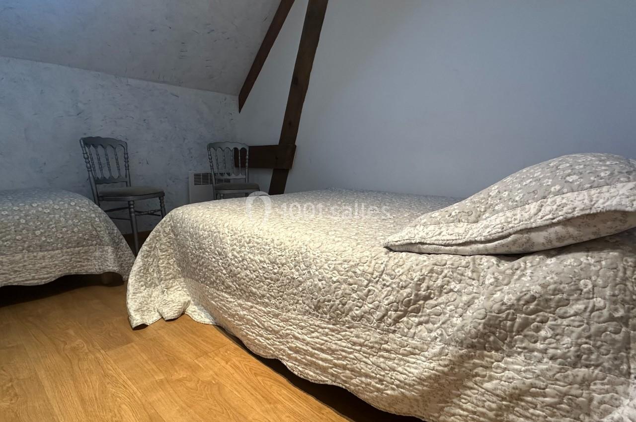 Deux lits simples avec couvre-lits texturés dans une chambre mansardée au sol en bois et murs clairs.