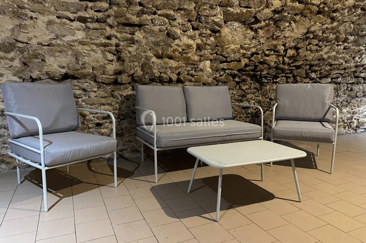 Mobilier de salon de jardin avec deux fauteuils, un canapé et une table basse, disposés sur un sol carrelé devant un mur en…