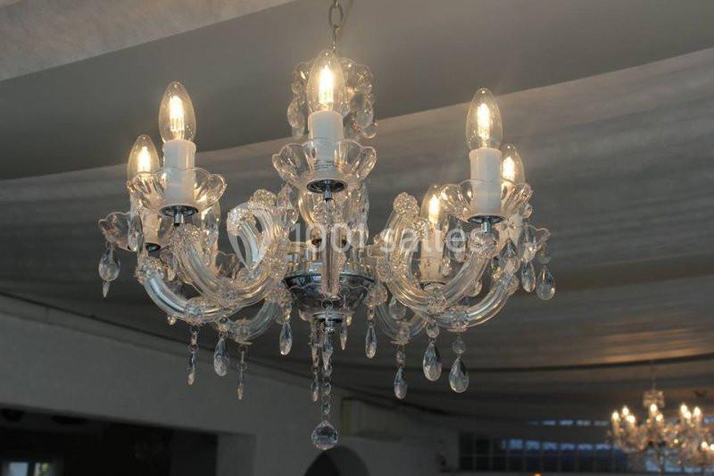 Lustre en cristal transparent avec plusieurs ampoules allumées, suspendu dans une pièce au plafond clair.